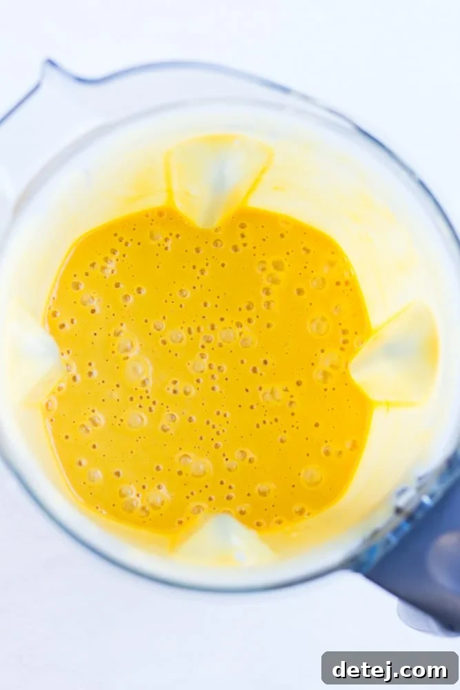 A high-speed blender container filled with a vibrant, creamy yellow vegan cheese sauce, showcasing its smooth texture before serving. This nut-free recipe yields a perfectly blended consistency.