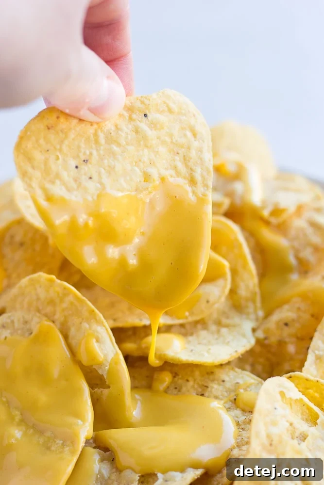 A single crispy tortilla chip generously coated with a rich, golden vegan cheese sauce, ready to be enjoyed. This image highlights the perfect consistency of the nut-free sauce for dipping.