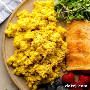 Close up on a pile of yellow tofu scramble on a plate with toast, greens, and berries.