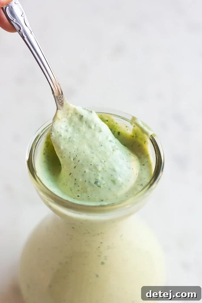 Luscious Vegan Green Goddess Dressing 2 Lush green vegan goddess dressing in a elegant white dish with a spoon, ready to serve.