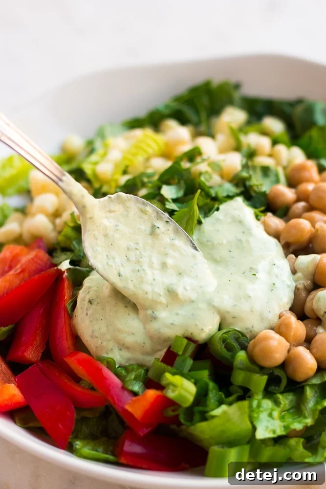Luscious Vegan Green Goddess Dressing 3 Vegan Green Goddess dressing being drizzled generously over a fresh salad, illustrating its perfect consistency.