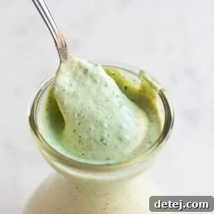 Lush green vegan goddess dressing in a elegant white dish with a spoon, ready to serve.