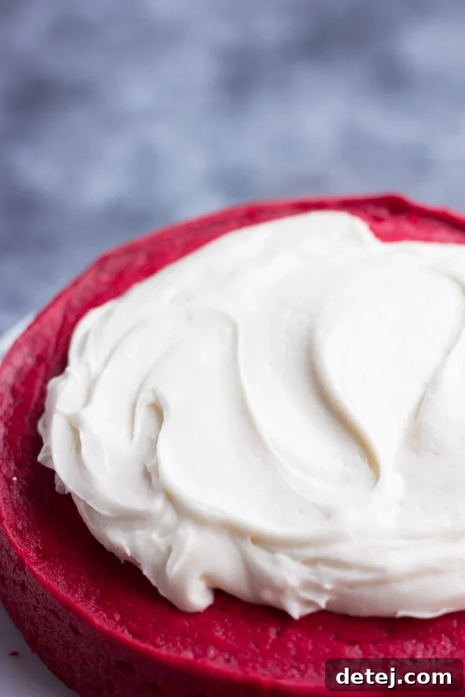 Lush vegan cream cheese frosting being expertly spread onto a rich red cake, highlighting its thick and creamy texture.