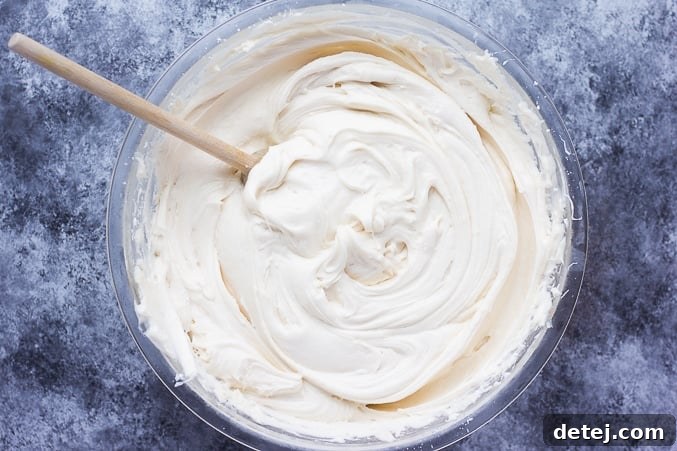 A beautifully textured bowl of freshly made vegan cream cheese frosting, ready to be spread, with a wooden spoon resting inside.