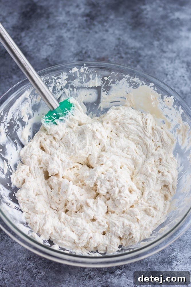 A stand mixer actively blending vegan cream cheese and butter in a bowl, creating a smooth, cohesive mixture.