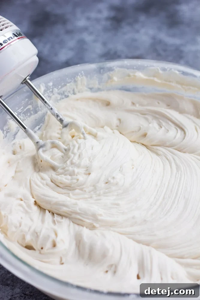 A bowl of vegan cream cheese frosting, now visibly thick and firm after chilling, with a mixer resting inside, ready for use.