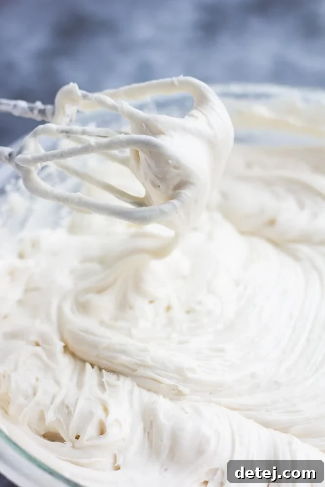 A close-up view of thick, white vegan cream cheese frosting being mixed in a bowl with an electric mixer.