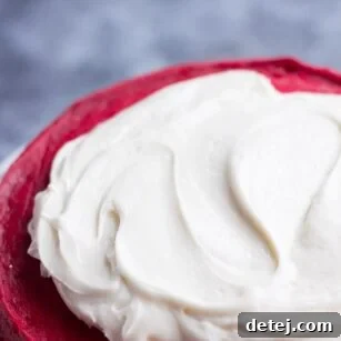 vegan cream cheese frosting being spread on a red cake.