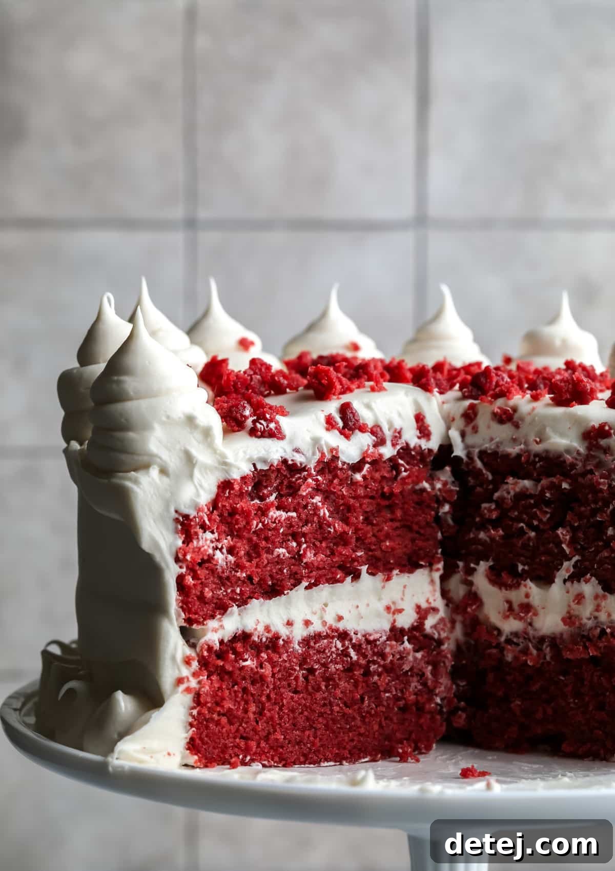 Ruby Red Vegan Indulgence 2 A stunning slice of Vegan Red Velvet Cake on a stand, showcasing vibrant red layers and luscious white frosting against a subtle grey background.