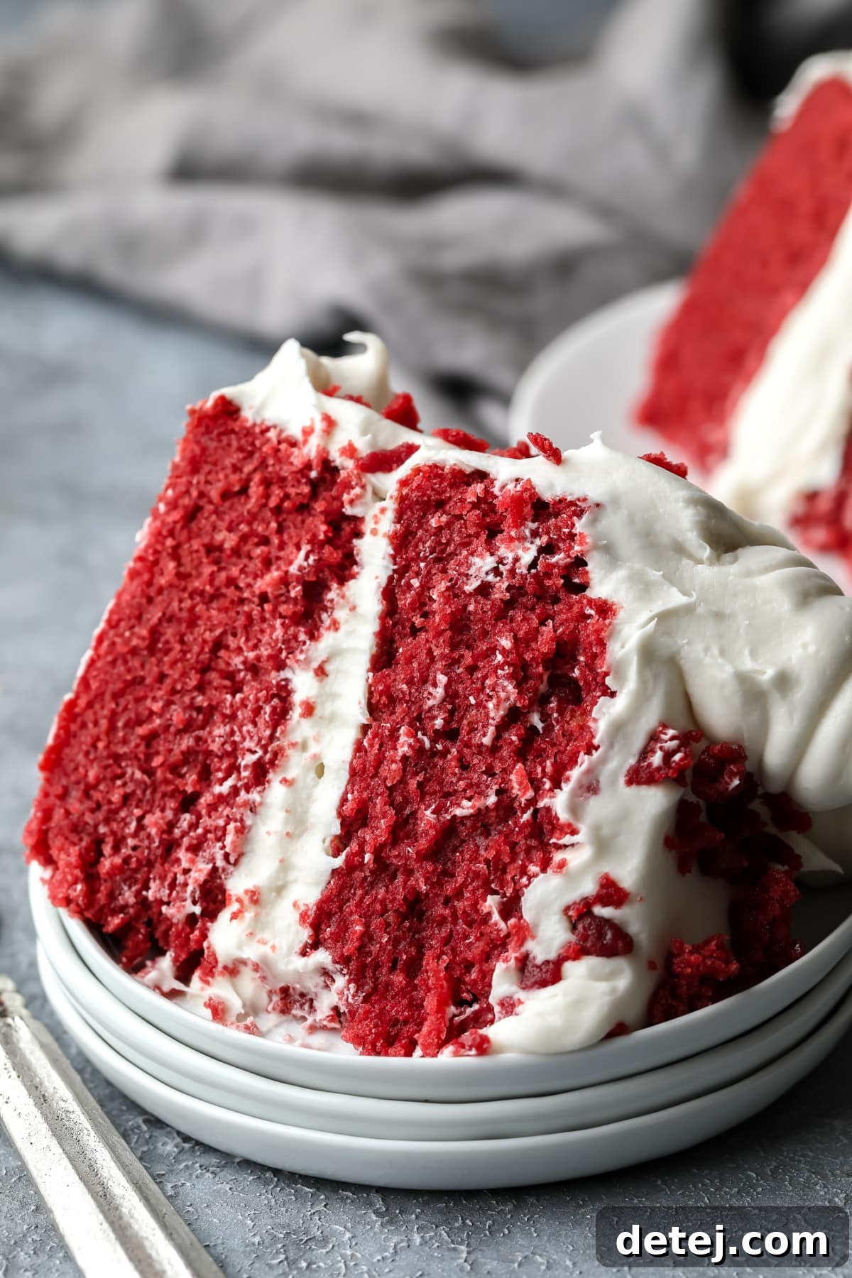Ruby Red Vegan Indulgence 3 A delectable slice of vegan red velvet cake, showcasing its vibrant red layers and rich cream cheese frosting, elegantly placed on a triple-tiered dessert plate.