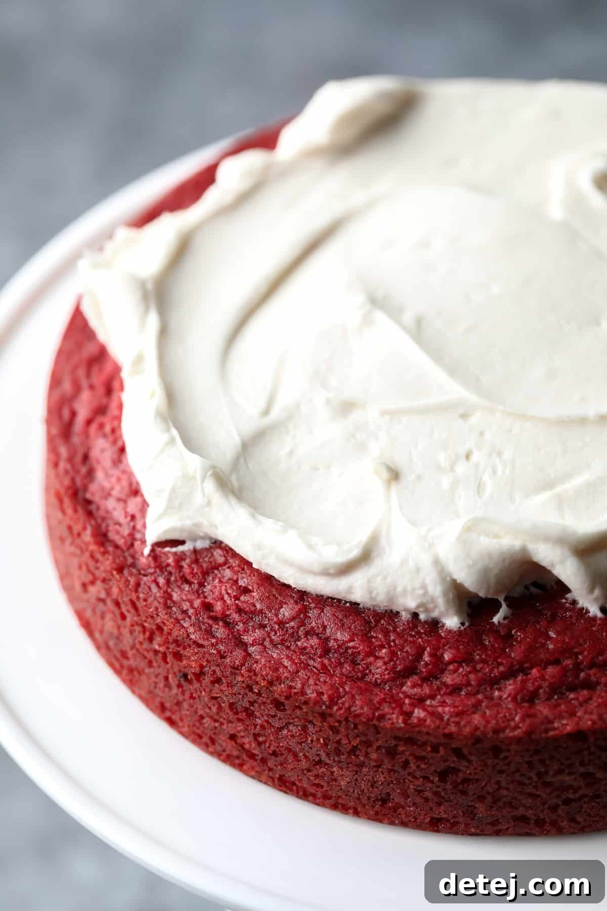 Ruby Red Vegan Indulgence 7 Smooth white frosting being expertly spread onto a vibrant red cake layer, demonstrating the process of assembling the vegan red velvet cake.