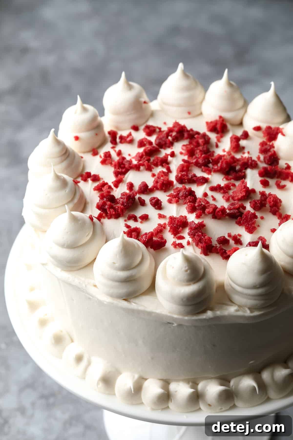 Ruby Red Vegan Indulgence 8 A beautifully frosted vegan red velvet cake, adorned with red cake crumbles and elegantly piped cream cheese frosting on top.