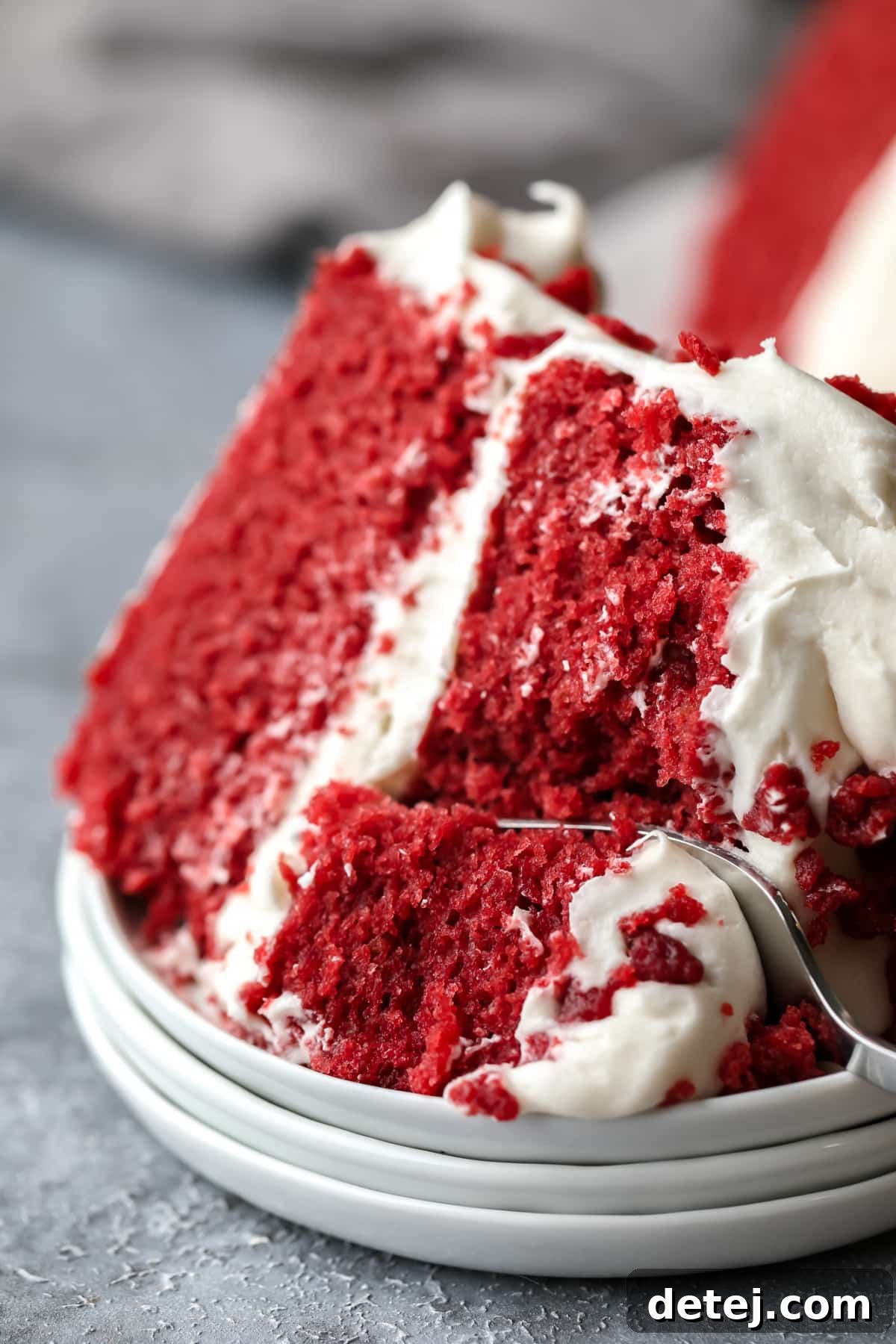 Ruby Red Vegan Indulgence 9 A fork taking a delicious bite out of a perfectly layered slice of vegan red velvet cake, showing its moist texture and creamy frosting.