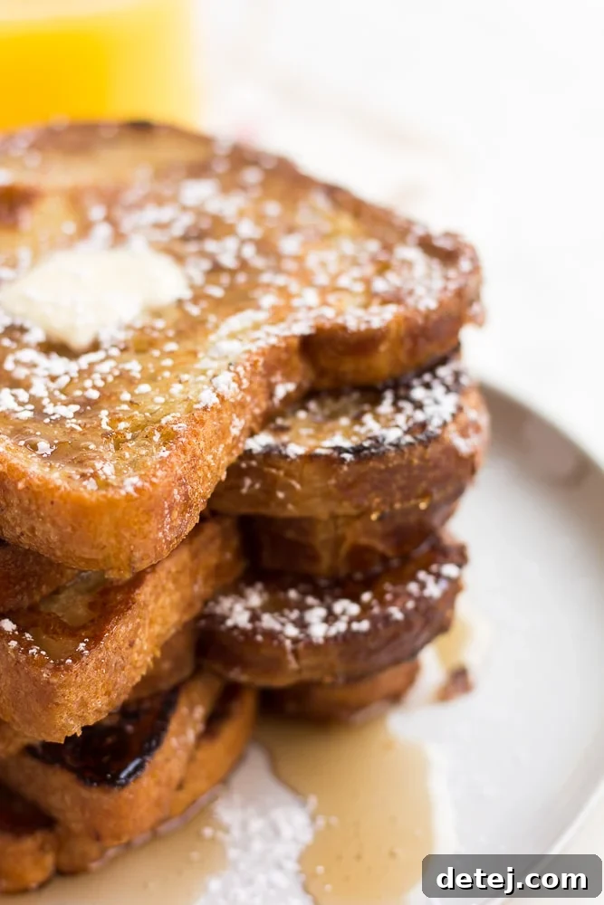 A stack of perfectly cooked vegan French toast adorned with a pat of butter, a dusting of powdered sugar, and a generous pour of maple syrup, inviting you to indulge.