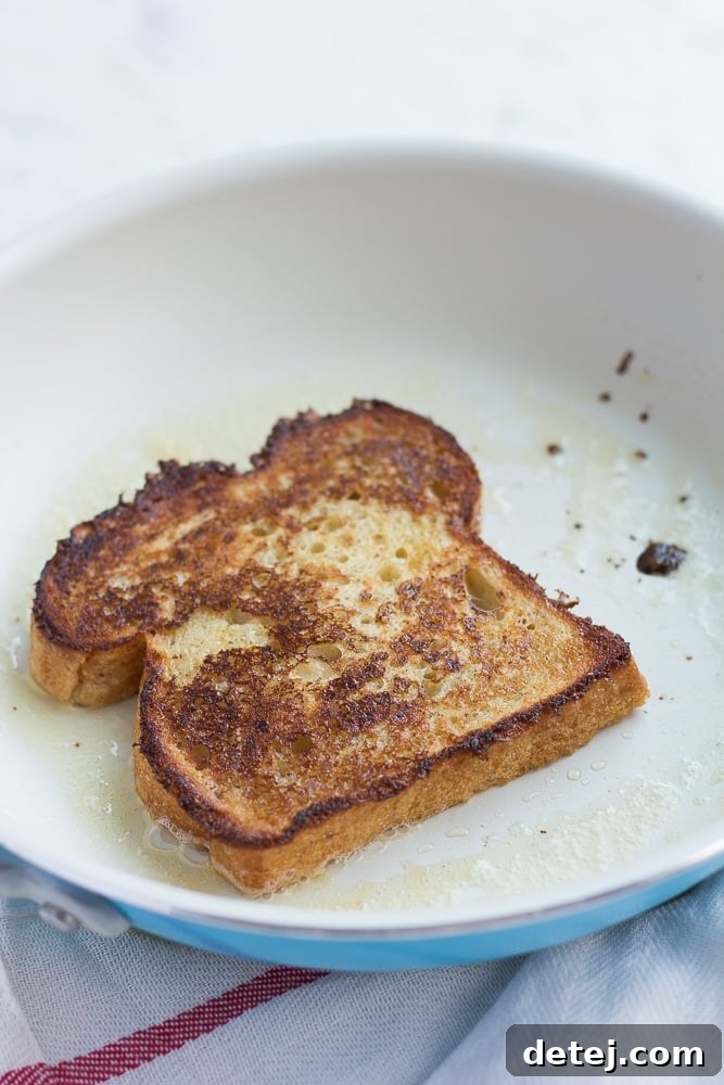 Several slices of vegan French toast cooking in a hot frying pan, turning golden brown and developing a crispy crust.