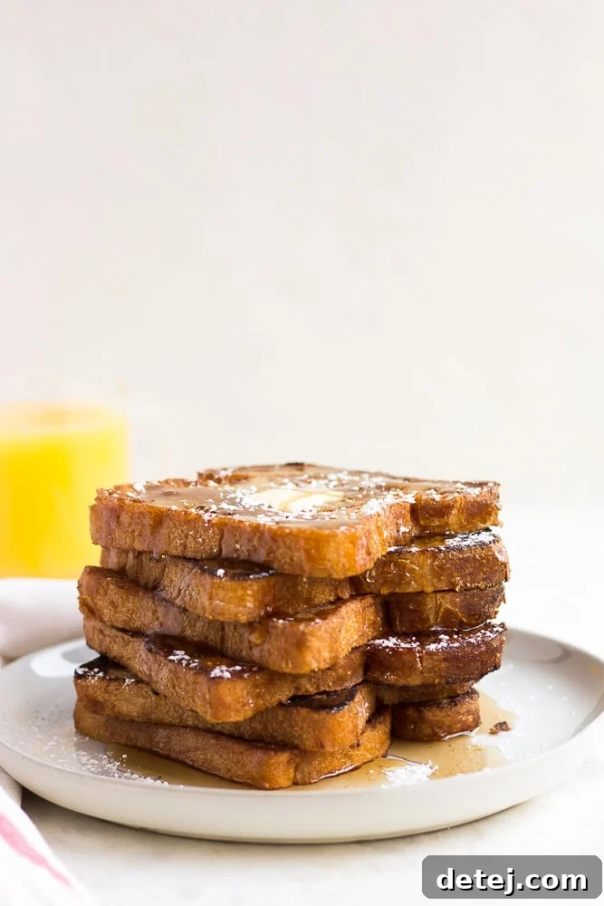 A beautifully arranged stack of golden-brown vegan French toast with a glass of orange juice in the background, making for a perfect breakfast scene.