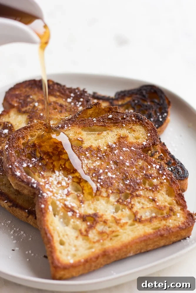 A plate of freshly cooked vegan French toast being generously drizzled with golden maple syrup, highlighting its appetizing appeal.