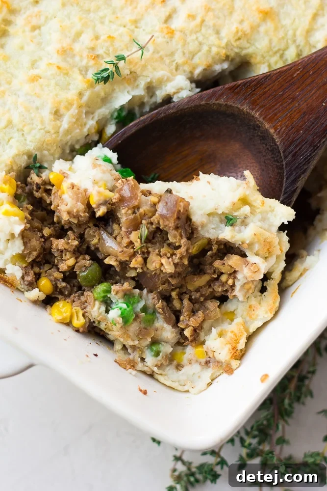 A wooden spoon serving a portion of vegan shepherd's pie from a casserole dish, highlighting the layers.