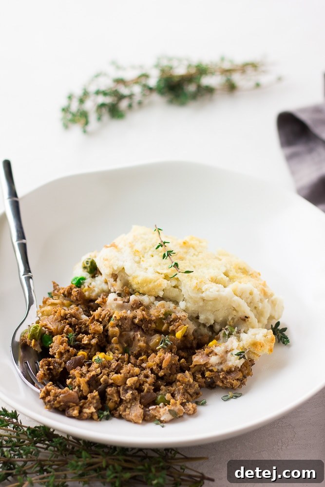 A serving of vegan shepherd's pie in a white bowl with a fork resting inside, showcasing the layers.