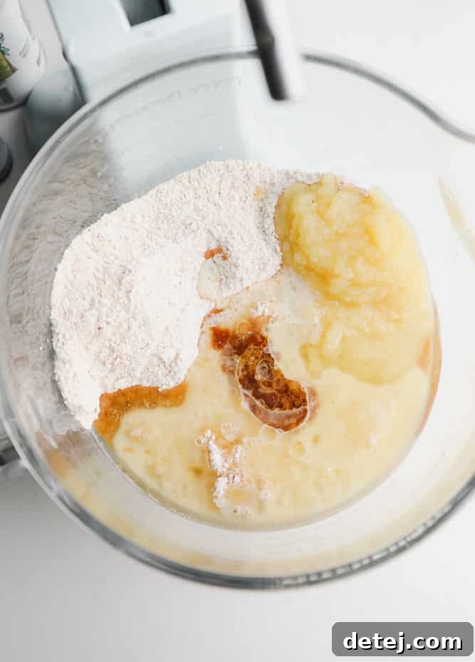 oil, applesauce and vanilla being added to dry ingredients in a bowl