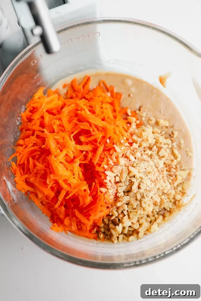 shredded carrots and walnuts being added to a clear bowl with batter