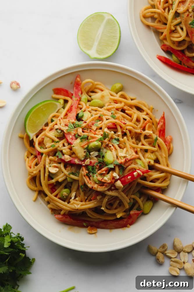 Two bowls brimming with vibrant Thai peanut noodles and an array of fresh vegetables.