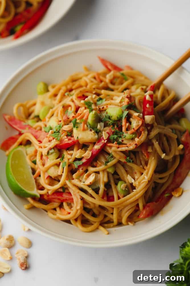 Close-up of a bowl of Thai peanut noodles garnished with fresh herbs, with chopsticks resting in the bowl, inviting a taste.