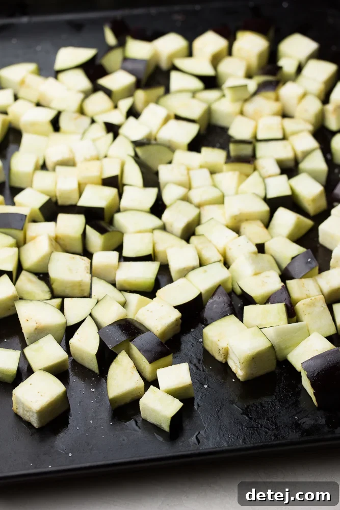 Freshly chopped eggplant, ready for roasting, on a clean wooden cutting board.