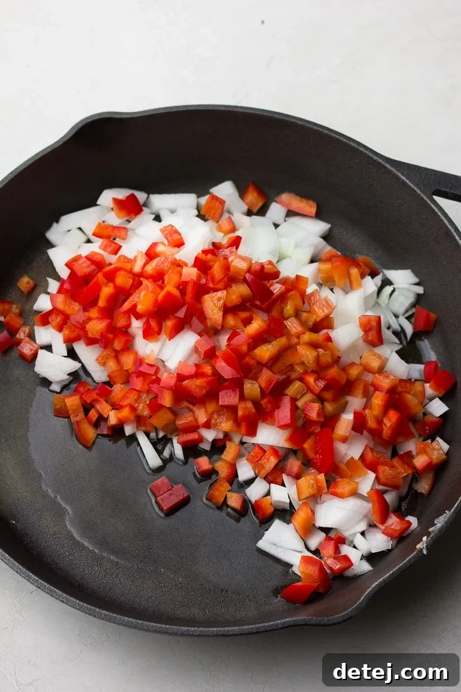 Uncooked, vibrant red bell peppers and yellow onions, freshly chopped and ready to be sautéed in a pan.