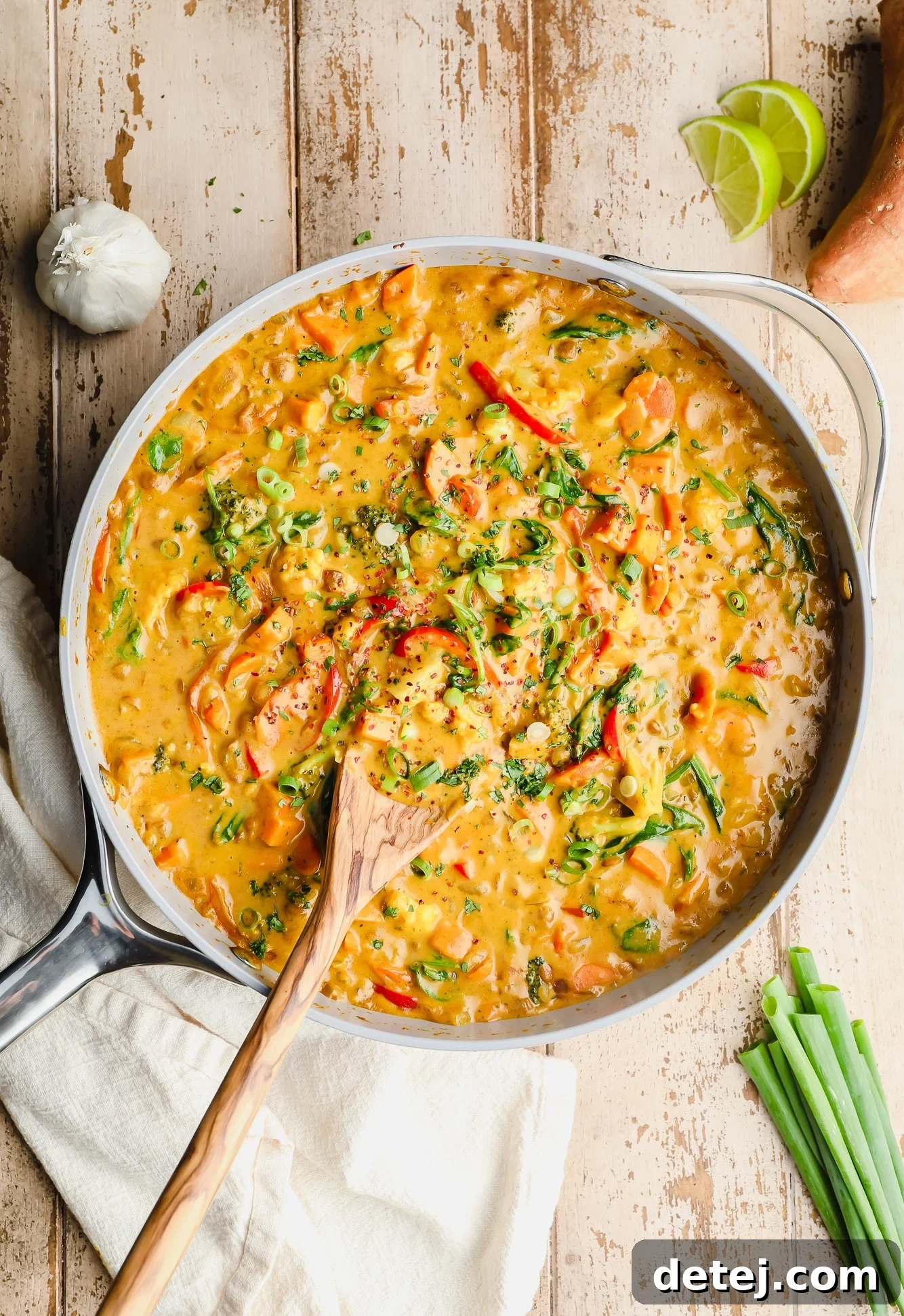 Quick and Flavorful Vegan Curry 3 A large grey pot filled with simmering vegan curry, with a wooden spoon stirring the vibrant mixture of vegetables, lentils, and creamy sauce.