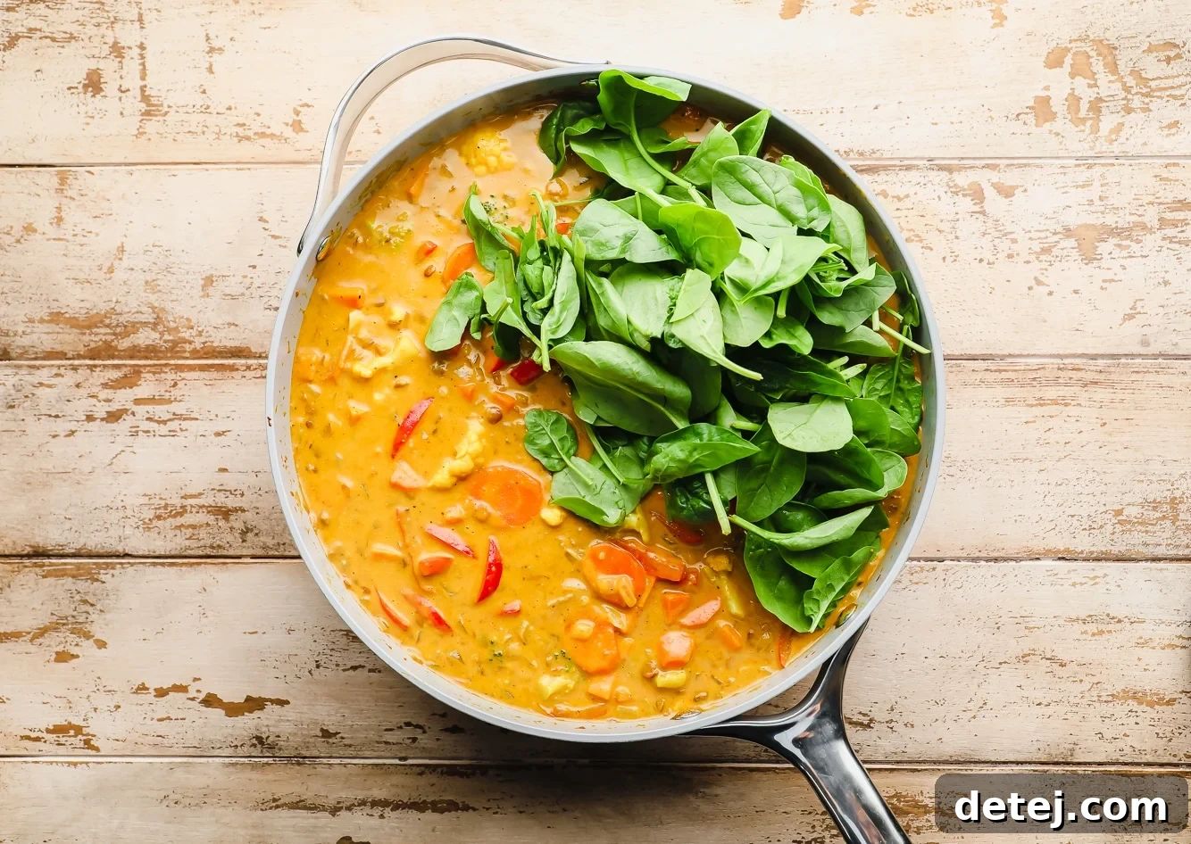Quick and Flavorful Vegan Curry 7 Fresh baby spinach being added to a simmering batch of vegan curry in a large grey pot, ready to wilt into the vibrant sauce.