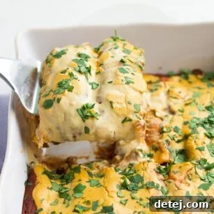 A vegan enchilada being lifted from a casserole dish, topped with red sauce and cheese.
