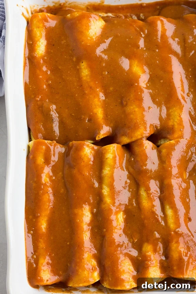 Ultimate Vegan Enchiladas 8 A casserole dish filled with rolled tortillas, completely covered in a rich, red enchilada sauce, ready for the next layer.