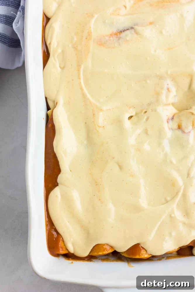 Ultimate Vegan Enchiladas 9 A casserole dish with enchiladas, now topped with a creamy white vegan cheese sauce over the red enchilada sauce, ready for baking.