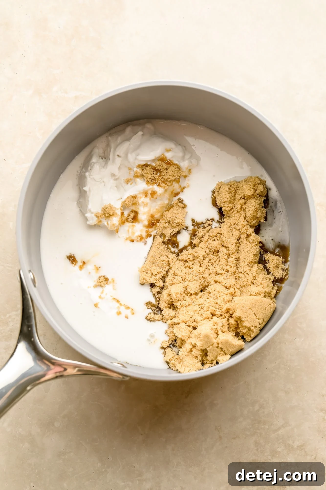 The two simple ingredients for vegan caramel, coconut cream and brown sugar, ready in a grey pot before cooking.
