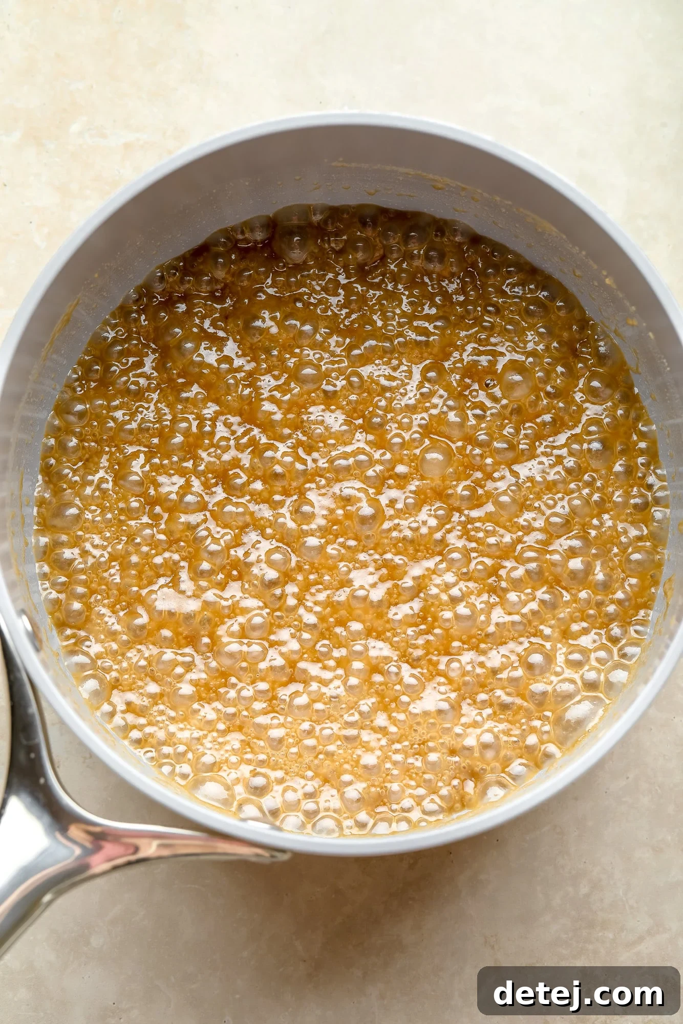 Rich vegan caramel sauce gently simmering in a grey pot on the stovetop, creating a smooth, golden texture.