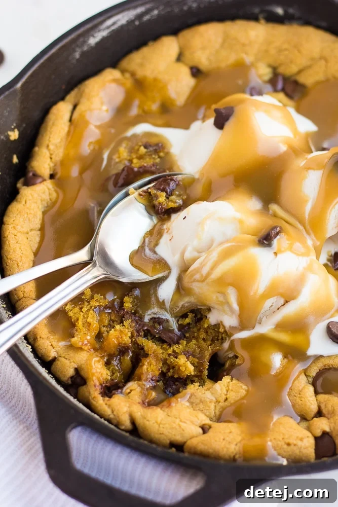 Warm vegan salted caramel skillet cookie topped with melting vanilla ice cream, rich caramel sauce, and spoons, ready to be shared.