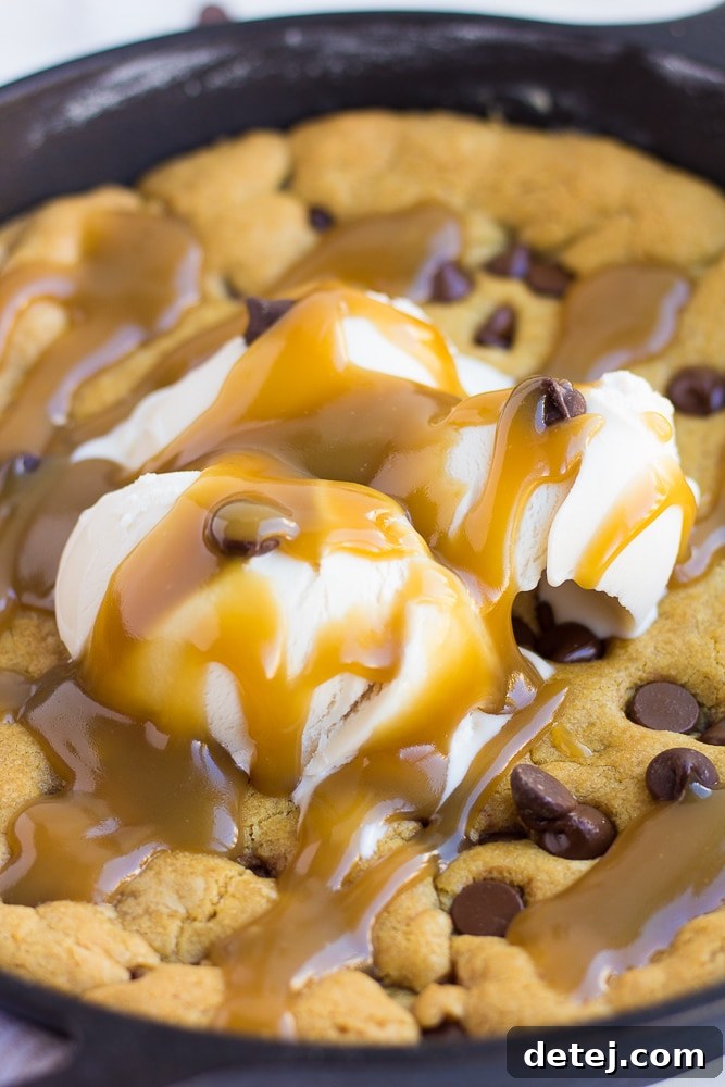 Close-up of a freshly baked vegan skillet cookie generously topped with scoops of non-dairy vanilla ice cream and glistening salted caramel.