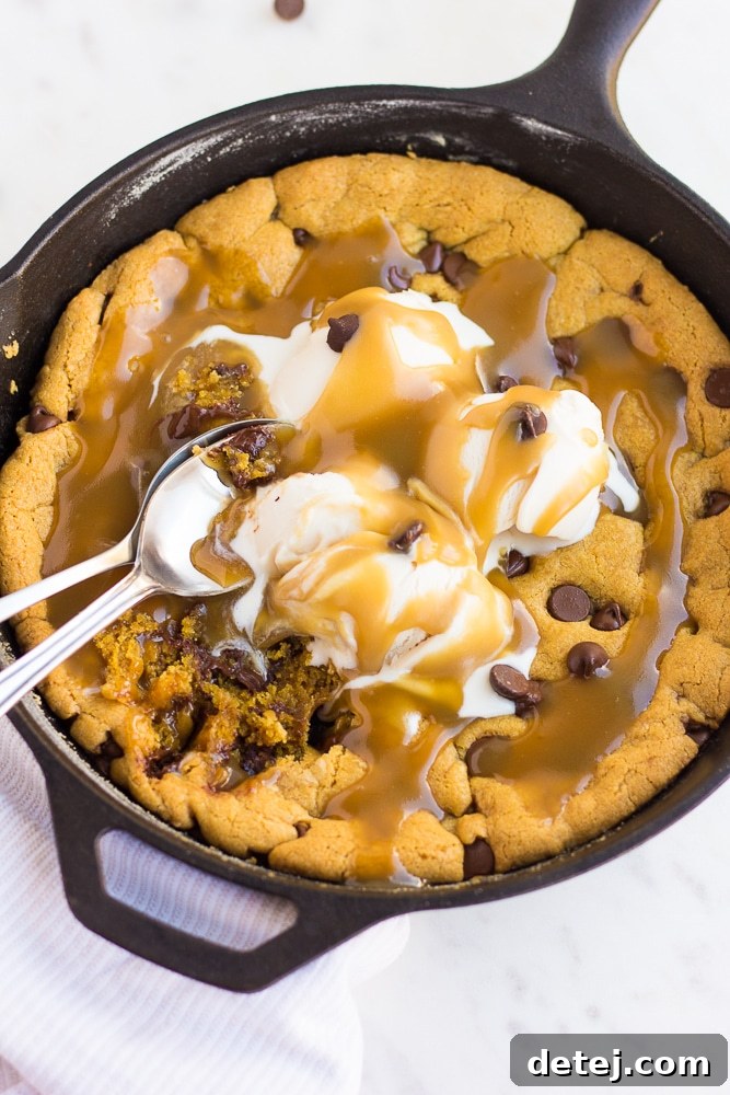 Top-down view of a vegan skillet cookie with scoops of melting non-dairy ice cream, salted caramel, and spoons, ready for immediate enjoyment.