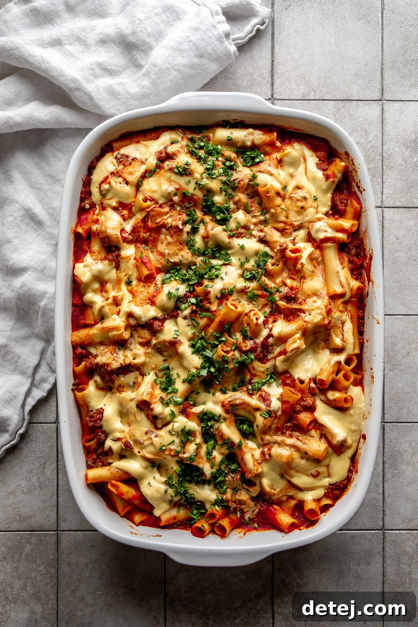 A large casserole dish filled with golden-brown Vegan Baked Ziti, generously topped with fresh parsley for garnish. The pasta is bubbly and inviting, showcasing its rich, comforting appeal.