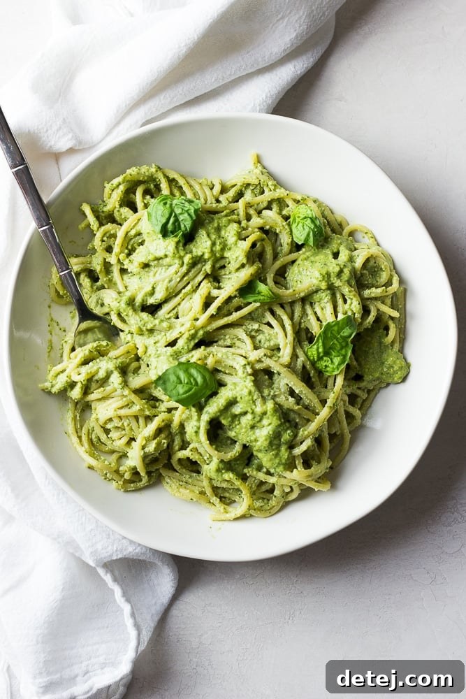 bowl of pasta drenched in pesto sauce, white bowl and background.