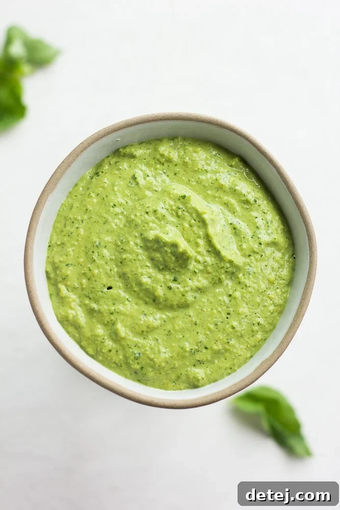 small bowl of vegan pesto, leaves of basil in background