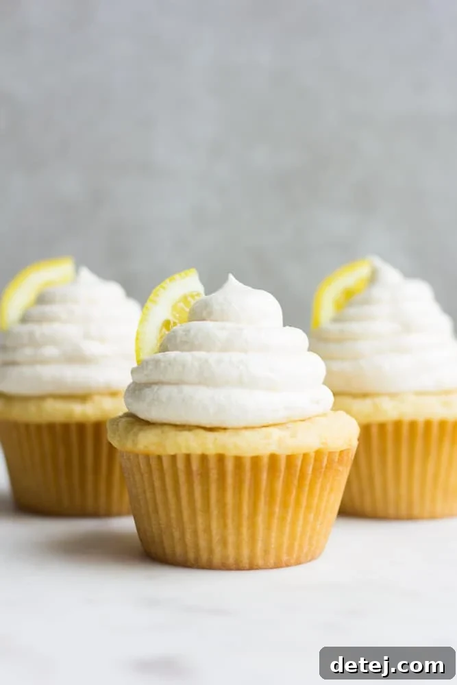 Bright and airy image of three beautifully frosted vegan lemon cupcakes, showcasing their soft texture and vibrant yellow hue.