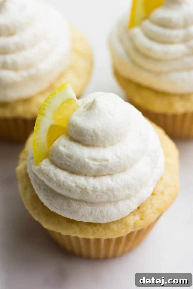 Overhead close-up of a single vegan lemon cupcake, revealing its fluffy buttercream frosting and a sprinkle of fresh lemon zest.
