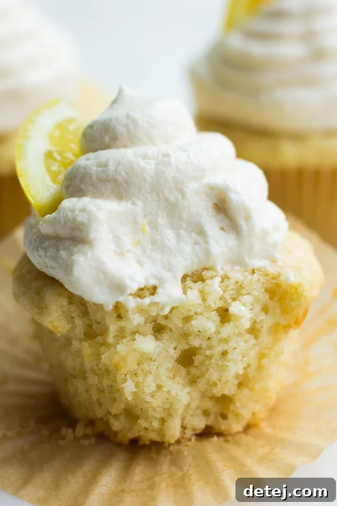 A vegan lemon cupcake with a bite taken out, revealing the moist yellow crumb and thick, creamy frosting.