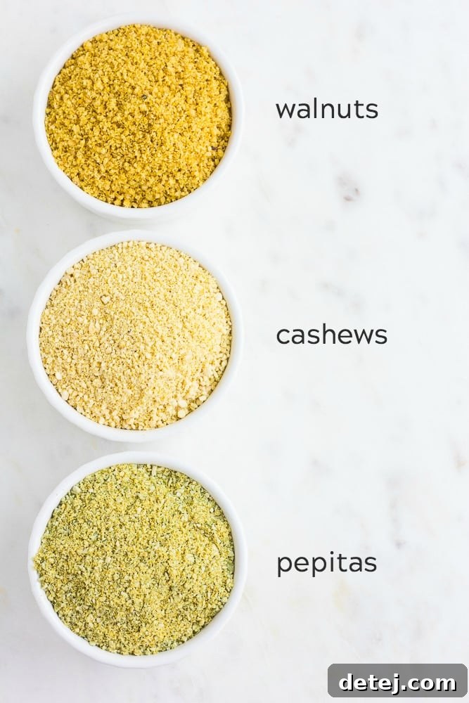 Three small bowls of vegan parmesan cheese, showing variations made with walnuts, cashews, and pepitas, arranged on a textured surface.