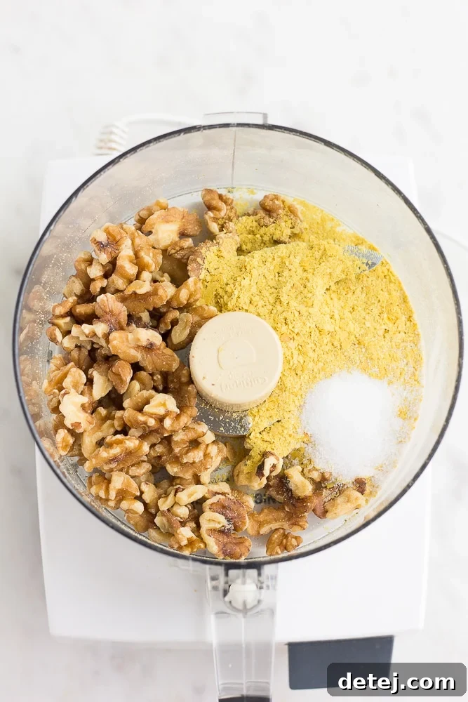 Close-up of raw walnuts, nutritional yeast, and salt in a food processor, before blending, illustrating the ingredients for walnut parmesan.
