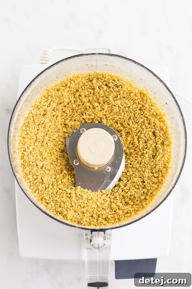 Finely pulsed walnut parmesan cheese in a food processor, showing its crumbly texture ready for use.