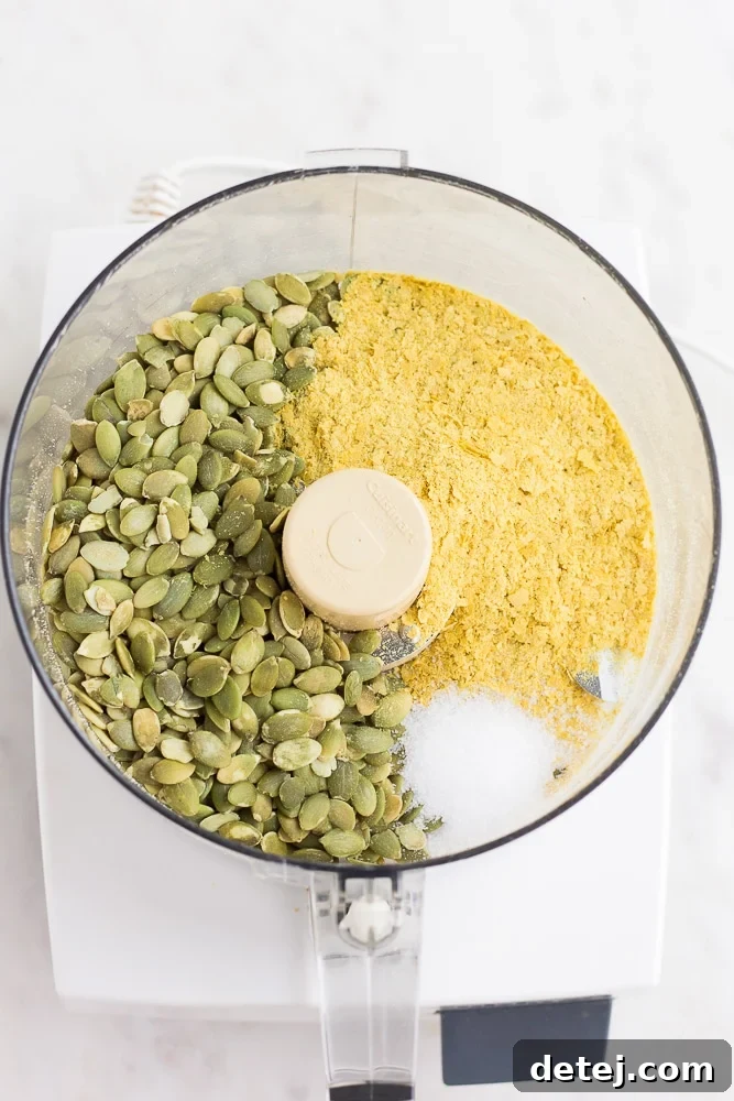 Raw pepitas, nutritional yeast, and salt in a food processor, ready for blending to make nut-free parmesan.