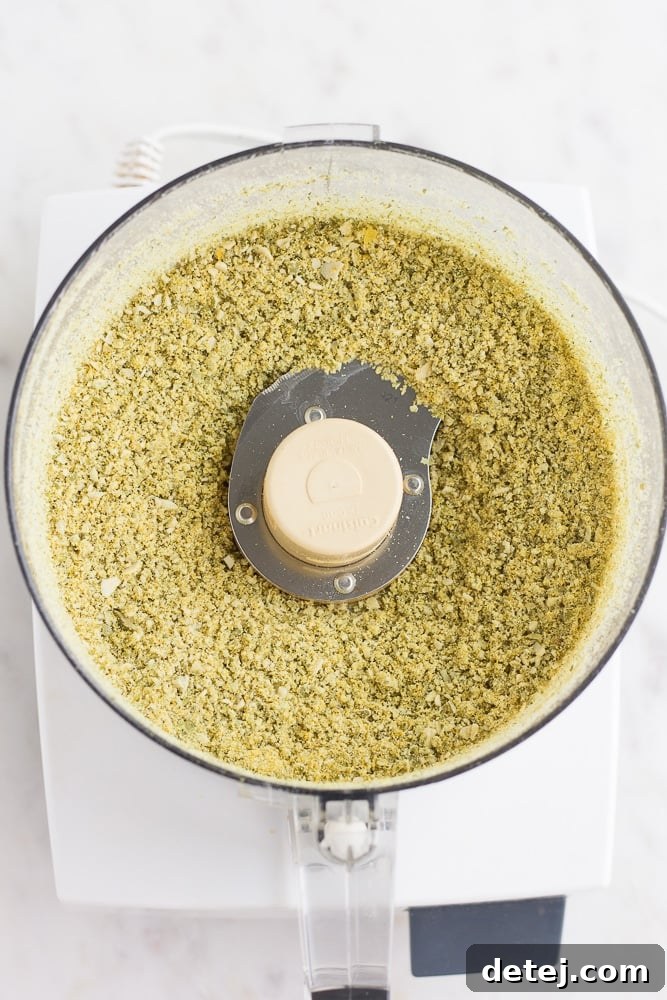 Finely processed pepita parmesan in a food processor, showcasing its perfectly crumbly texture, ideal for sprinkling.